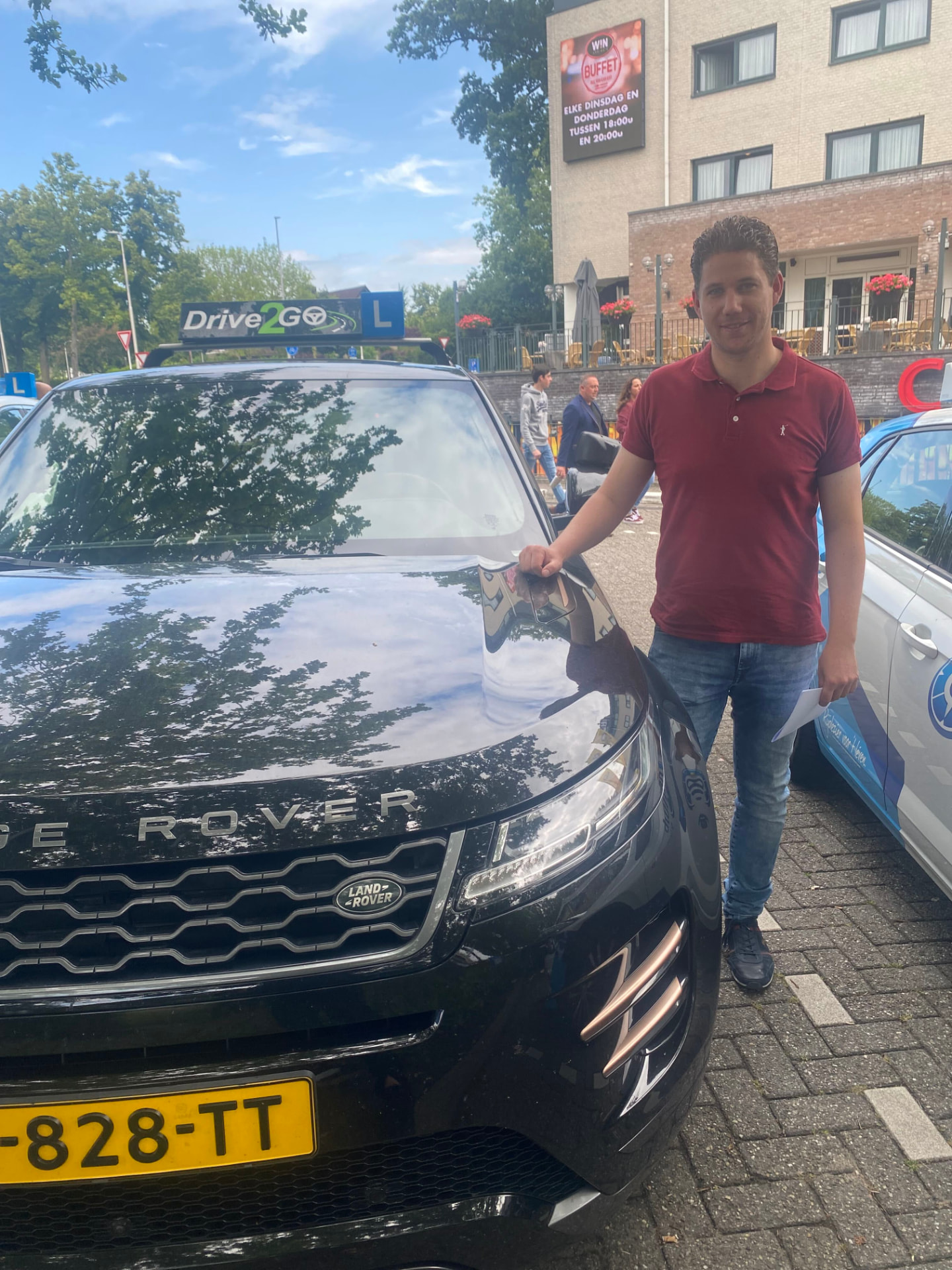 Geslaagde leerling bij de lesauto op het examenplein