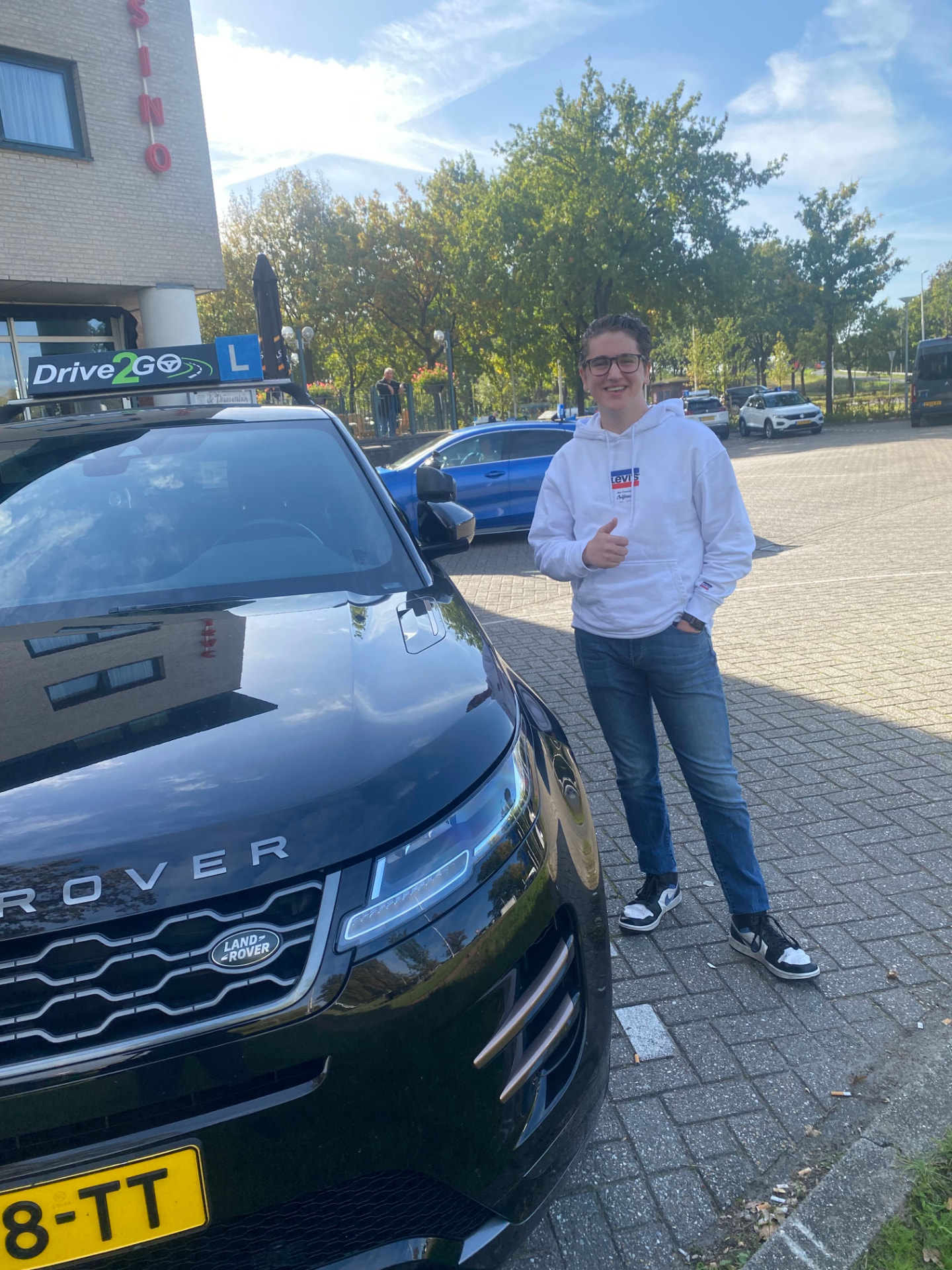 Geslaagde leerling met duim op bij de lesauto
